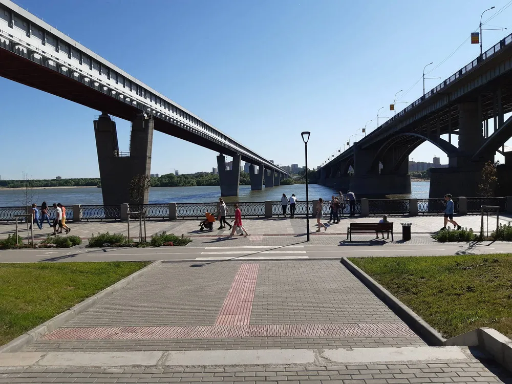 Люди гуляют по Михайловской набережной между двумя большими мостами в Новосибирске