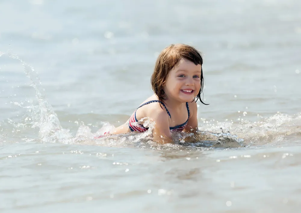 Маленькая девочка радостно плещется в воде на пляже