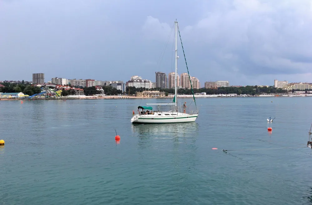 Белая яхта в Черном море на фоне набережной Геленджика