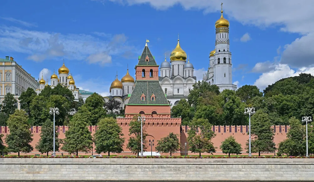 Соборы Московского Кремля возвышаются за Тайницкой башней и крепостной стеной на Кремлевской набережной в Москве